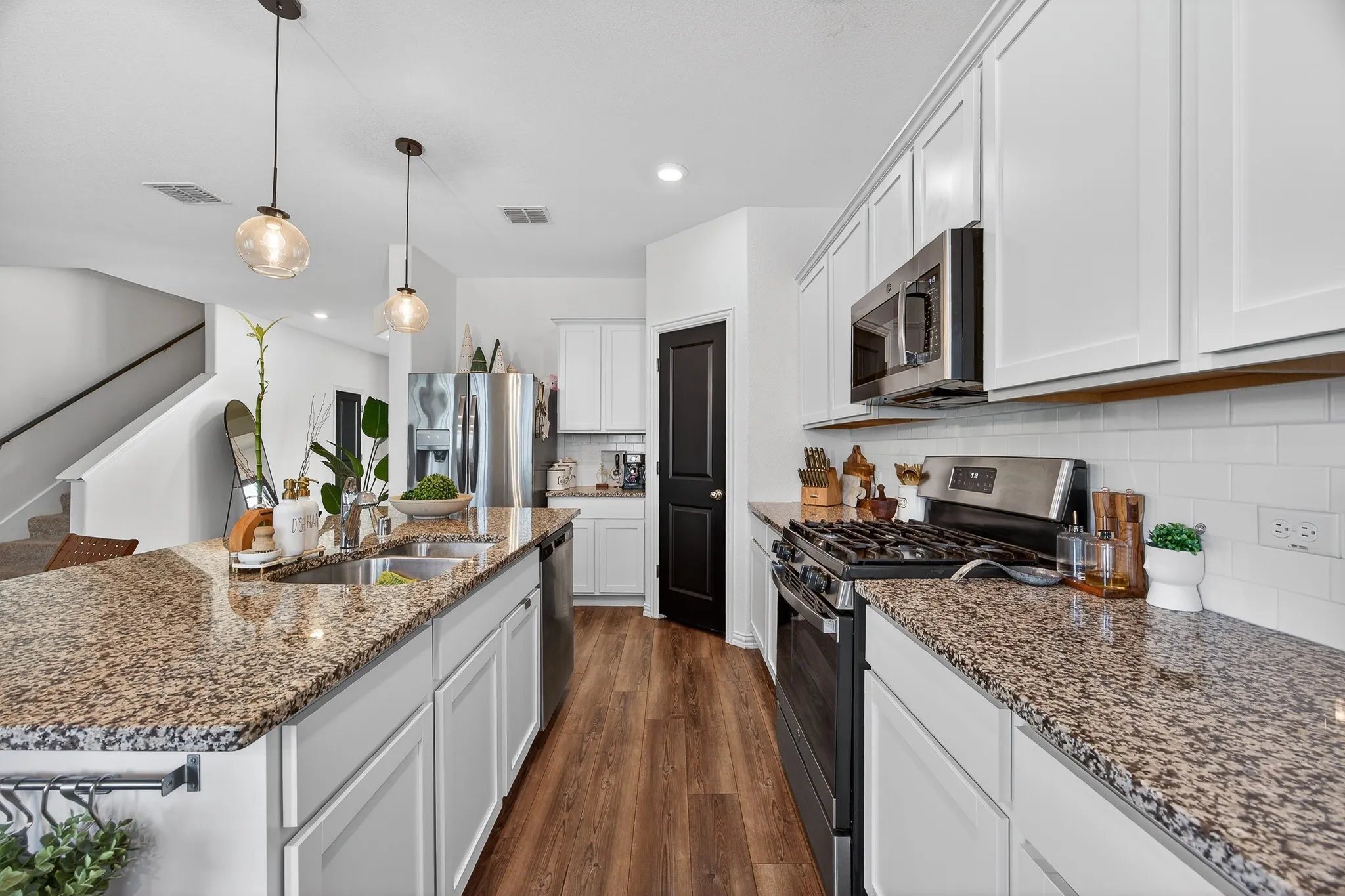Open-concept kitchen featuring an expansive island with a double sink, wood-finish flooring, white cabinetry, granite countertops, and stainless steel appliances