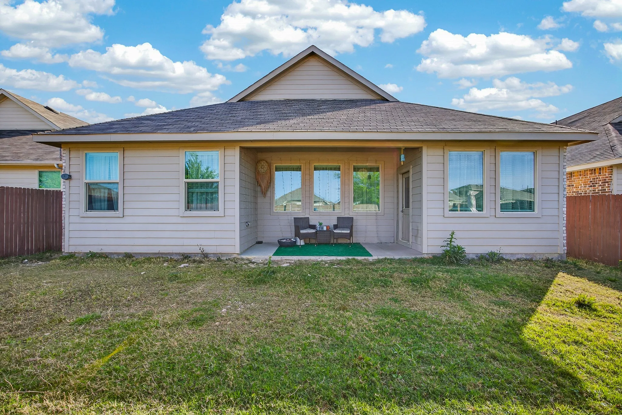 Rear exterior with a covered patio, multiple windows, and a fenced perimeter