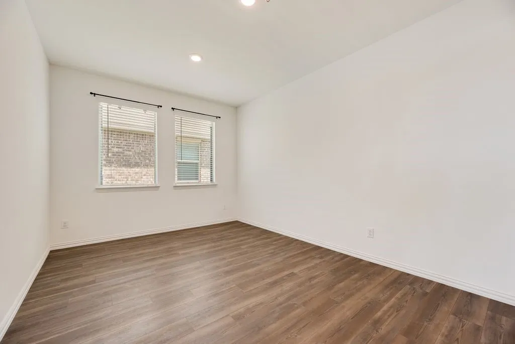 Bright room featuring two windows with blinds, recessed lighting, white walls, white baseboards, and wood-finish flooring