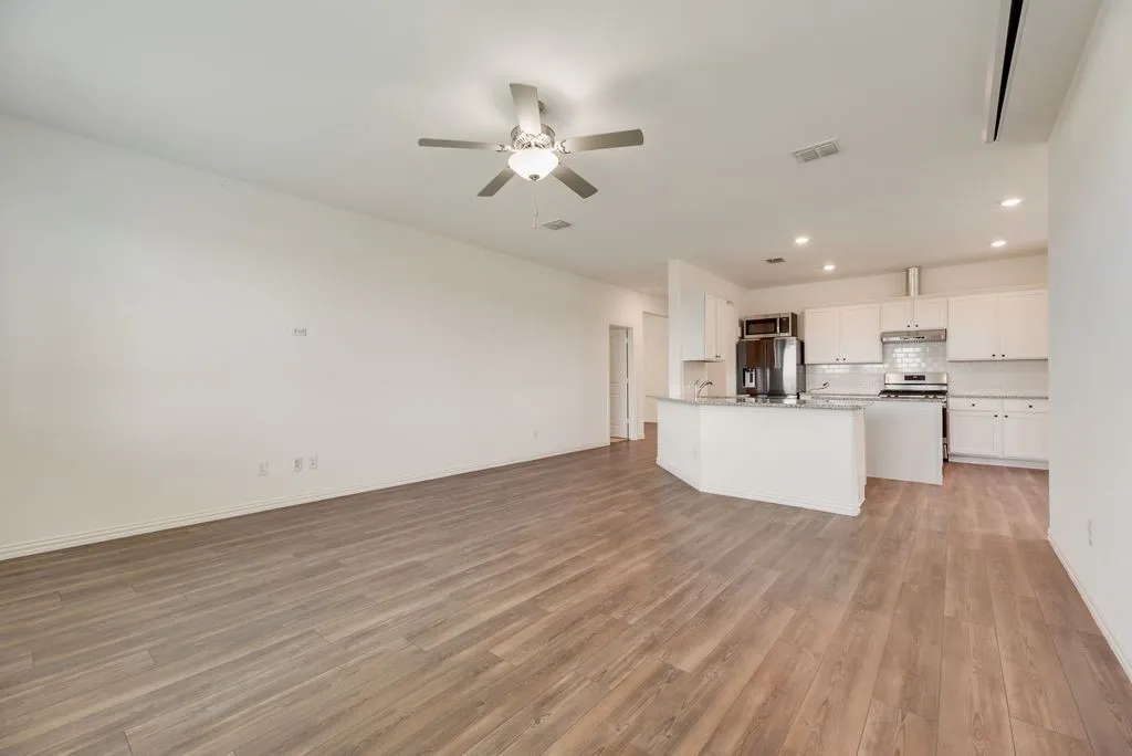 Spacious open-concept living area featuring wood-finish flooring and a ceiling fan with integrated lighting