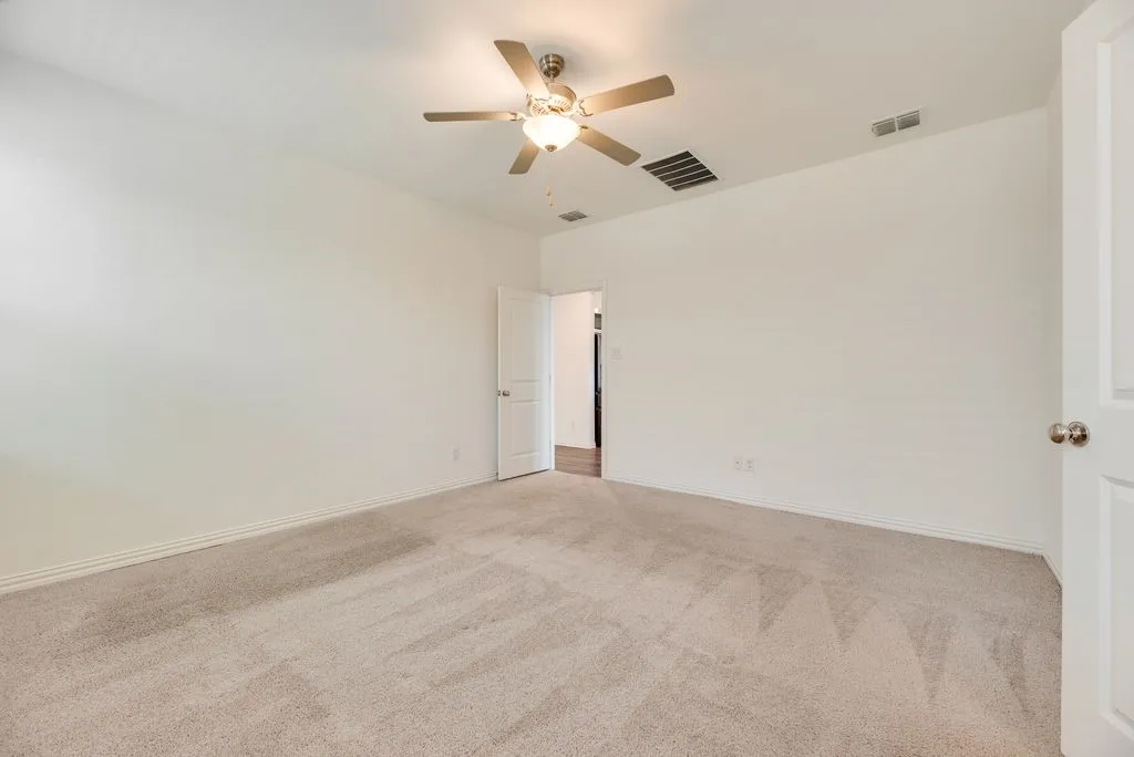 Spacious interior room featuring light-toned carpeting, neutral wall paint, and a ceiling fan with integrated lighting