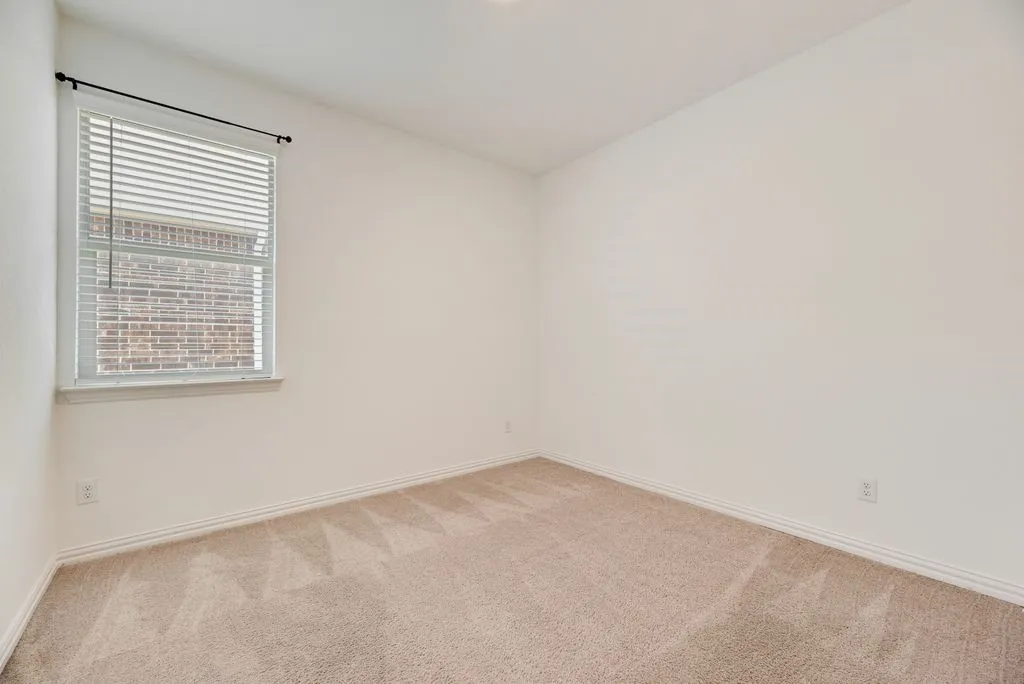 Carpeted room featuring a single window with blinds, white walls, and white baseboards