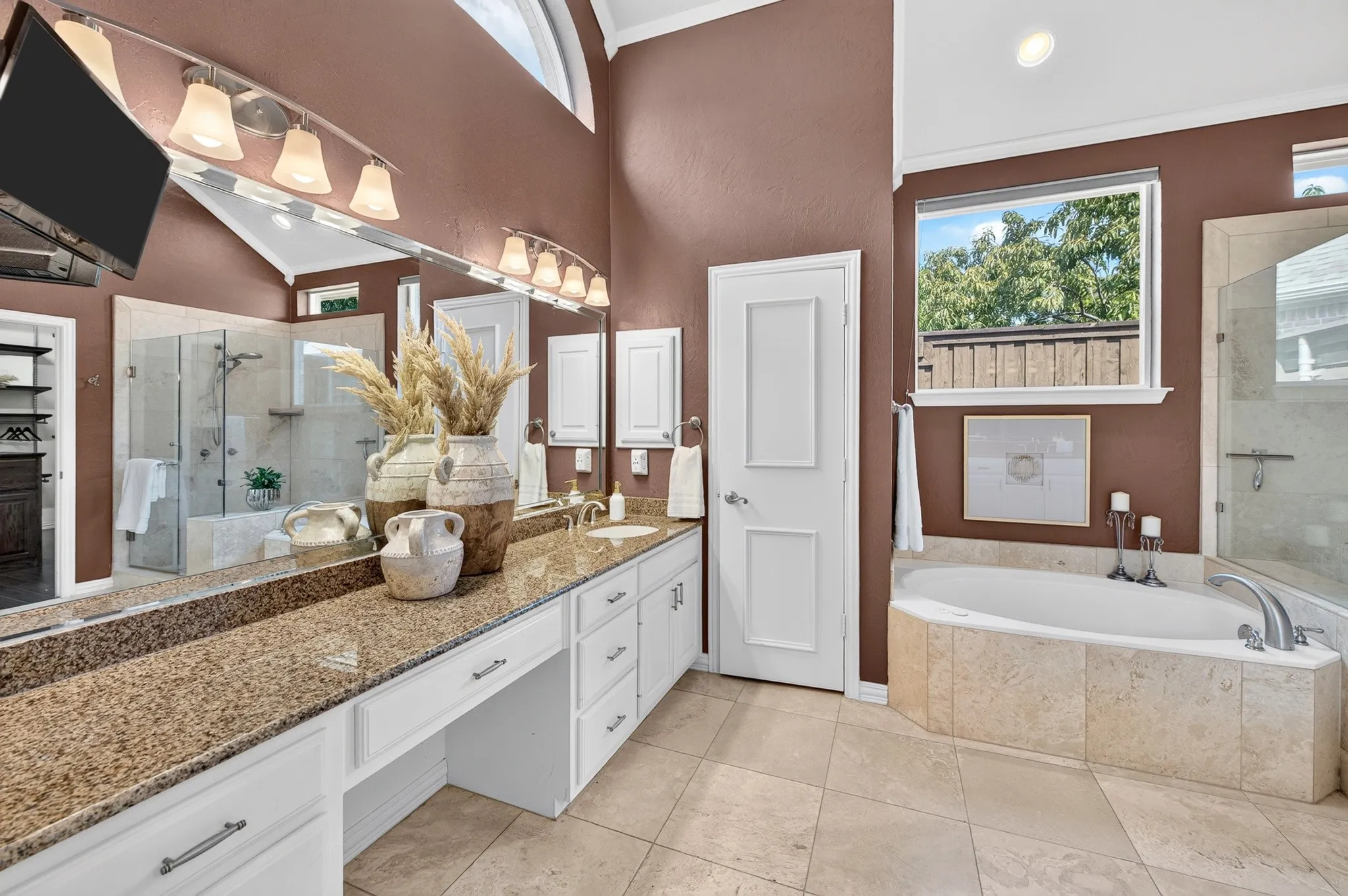 Vaulted ceiling bathroom featuring a built-in soaking tub, a frameless glass shower enclosure, a dual vanity with a granite countertop, and tile flooring
