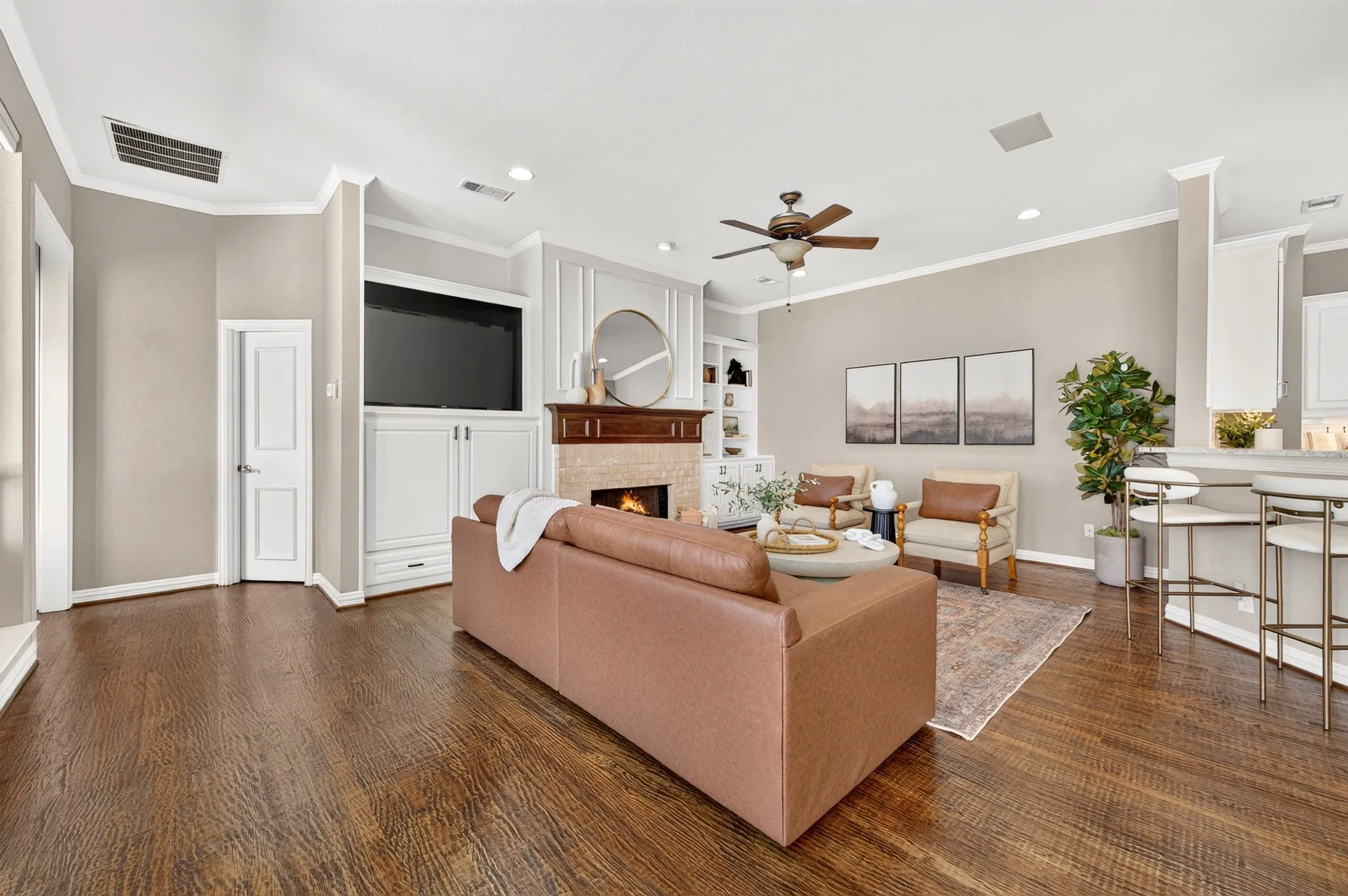 Wood-finish flooring, built-in cabinetry, crown molding, a ceiling fan with integrated lighting, and a fireplace with a wood mantel