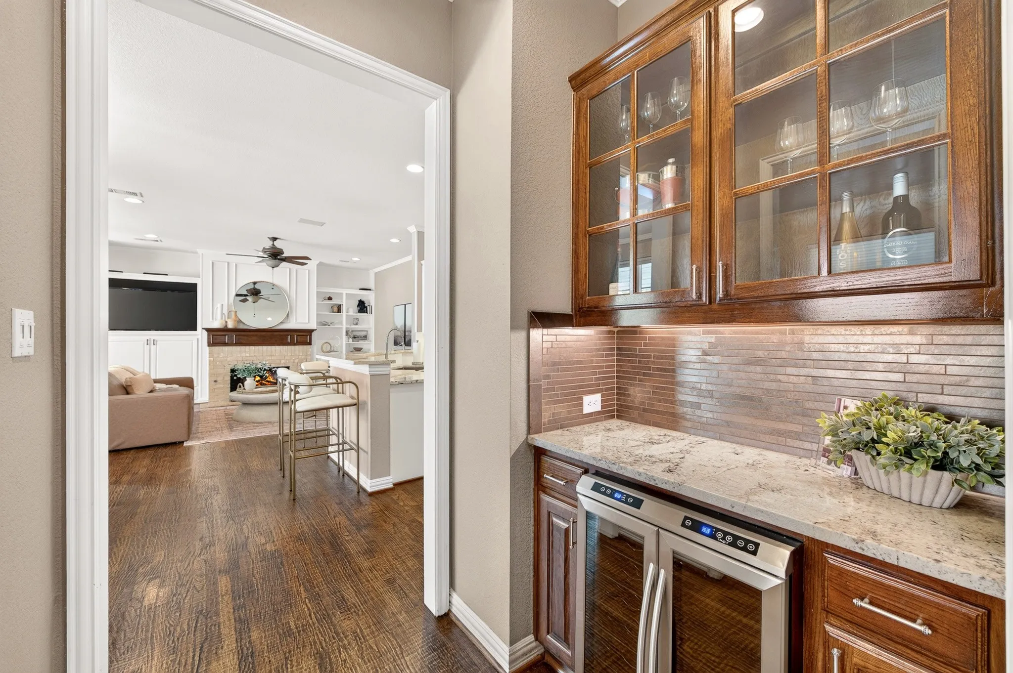 Built-in beverage cooler, wood-finish cabinetry, stone countertop, tile backsplash, and recessed lighting