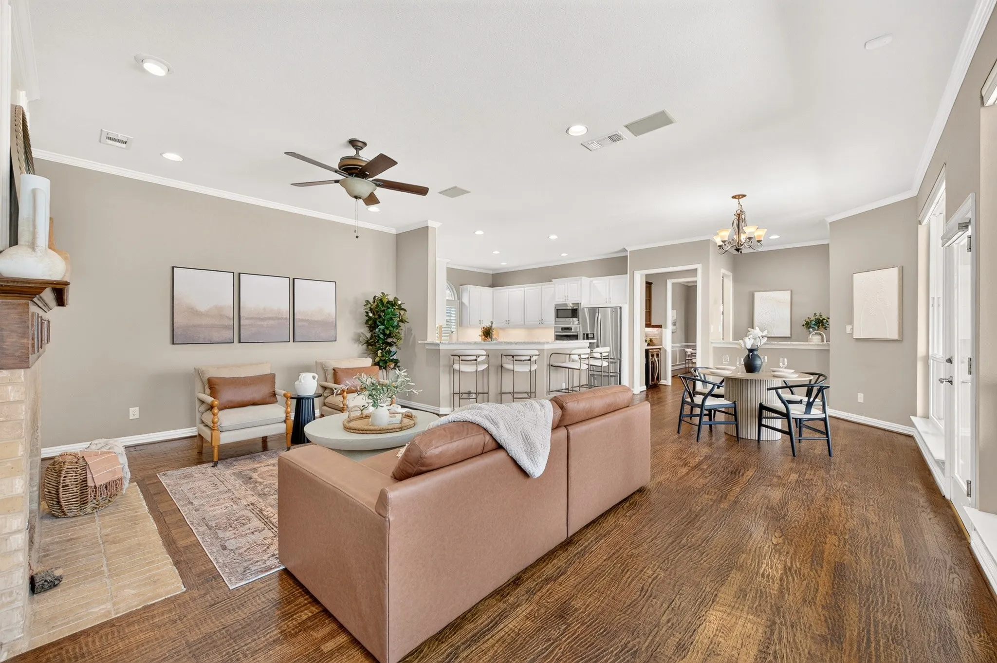 Open-concept living area with dark wood-finish flooring, a stone fireplace, and crown molding