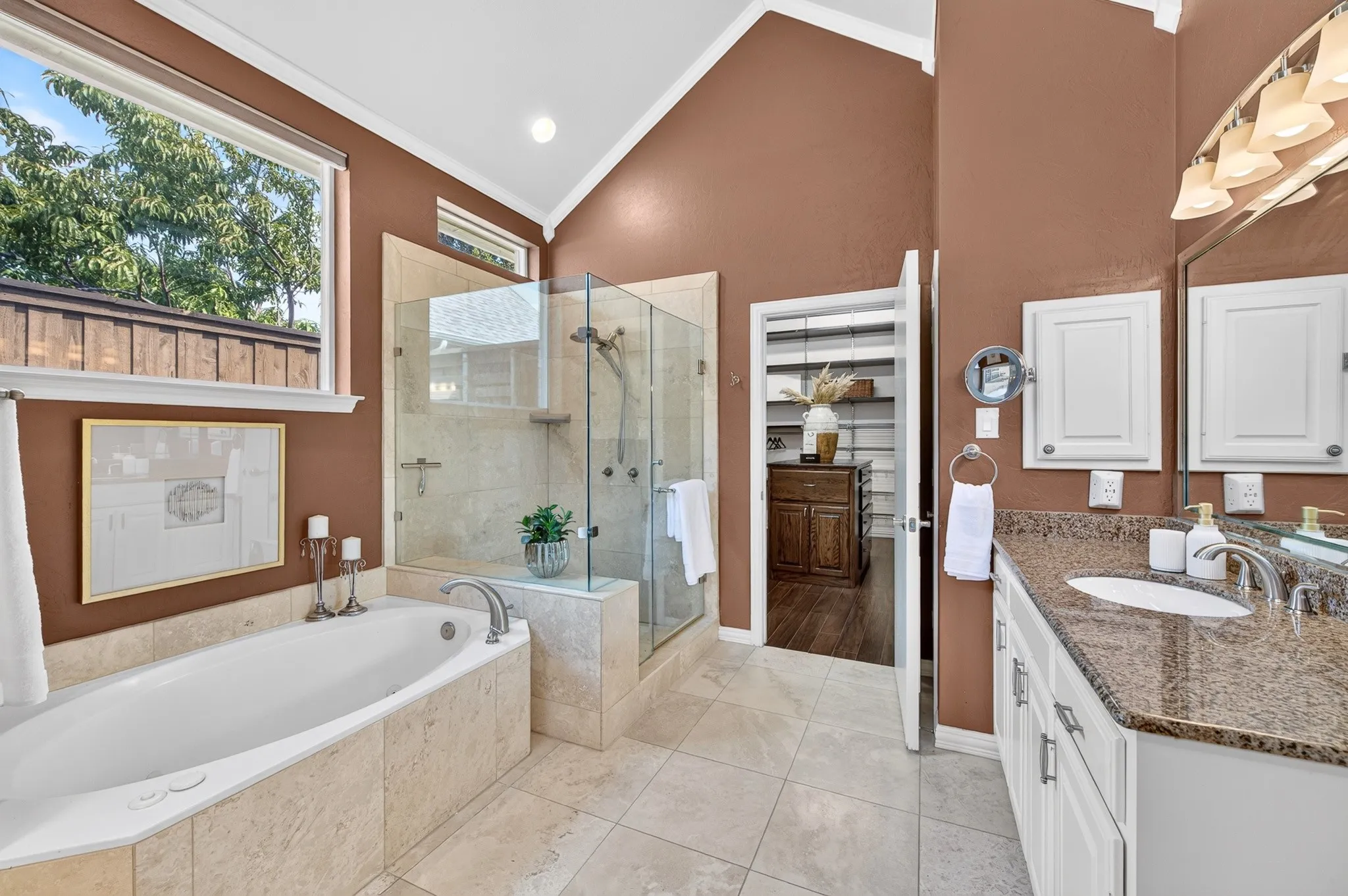 Vaulted ceiling bathroom featuring a built-in soaking tub, glass-enclosed shower, dual vanity with stone countertop, and tile flooring
