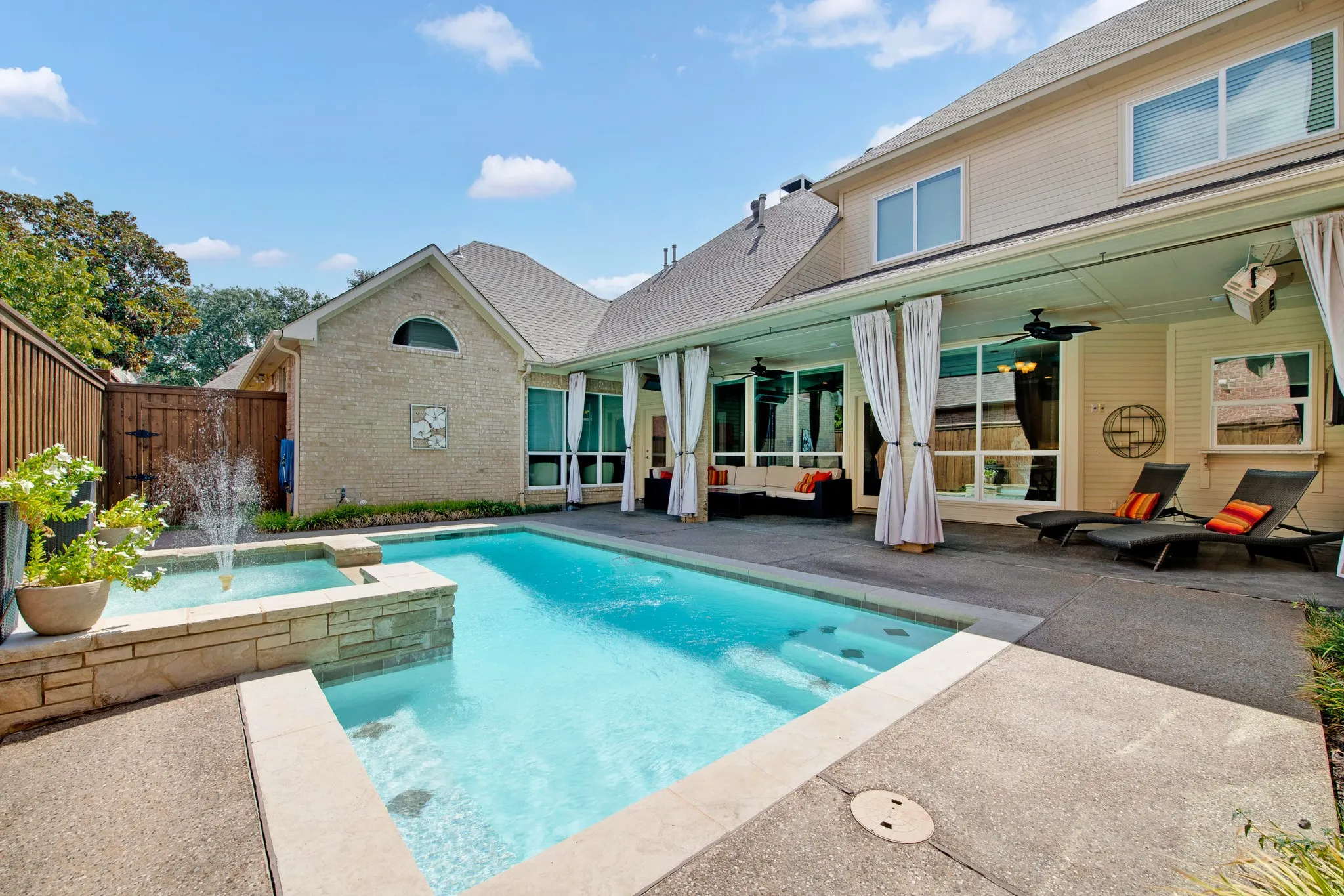 Backyard oasis featuring a swimming pool with integrated spa and waterfall, a covered patio with ceiling fans, and a privacy fence