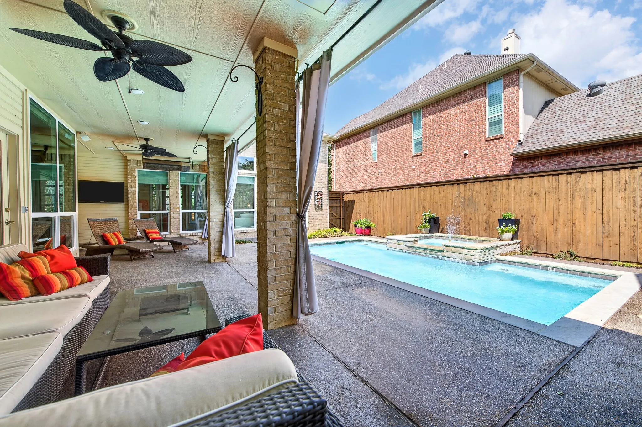 Covered patio with multiple ceiling fans, integrated lighting, and a swimming pool featuring a built-in spa with water features