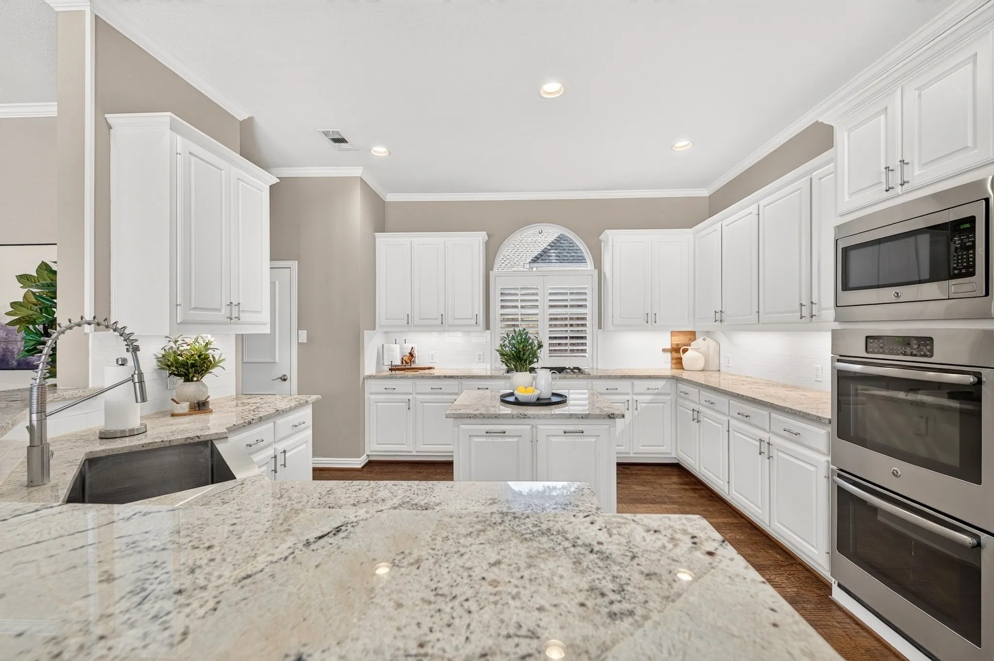 Kitchen featuring white cabinetry, light-toned countertops, a stainless steel sink with a gooseneck faucet, a built-in microwave, and a double oven