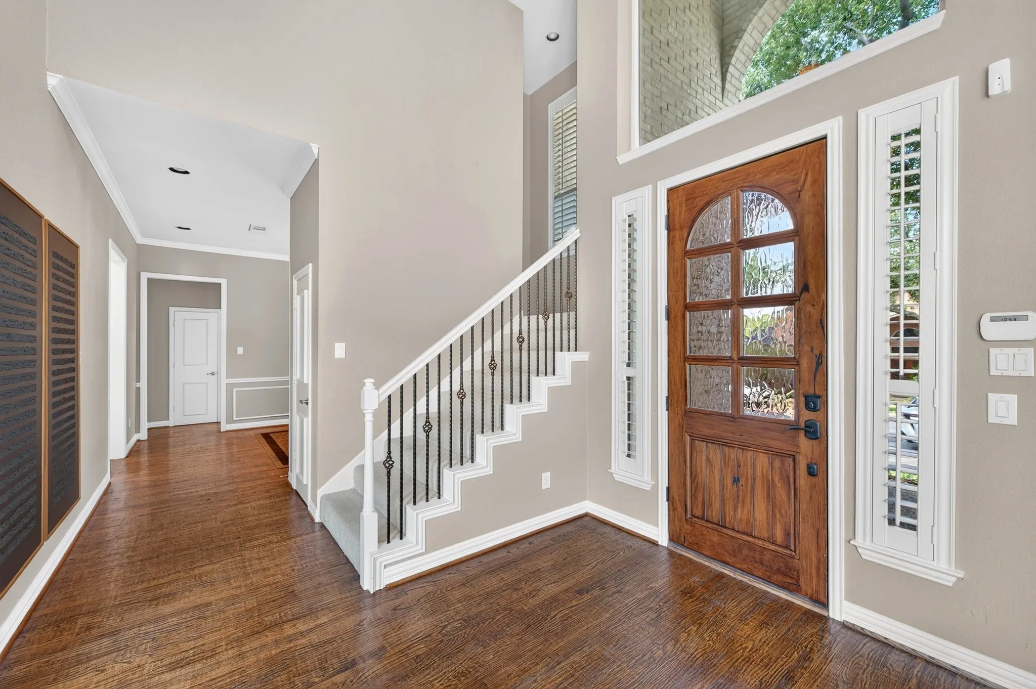 Hardwood flooring, arched wood-panel entry door with glass inserts, transom window, side-light windows with plantation shutters, and a staircase with wrought iron balusters