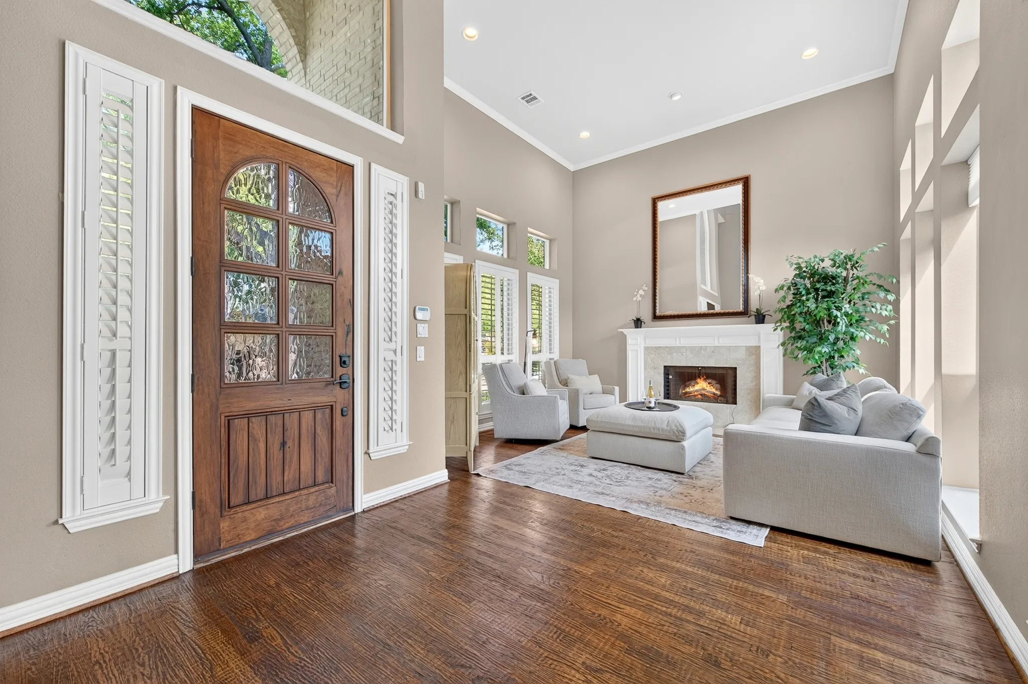 Hardwood flooring throughout the entry, a wood-paneled front door with glass inserts, high ceilings, a fireplace with a stone surround, and multiple windows