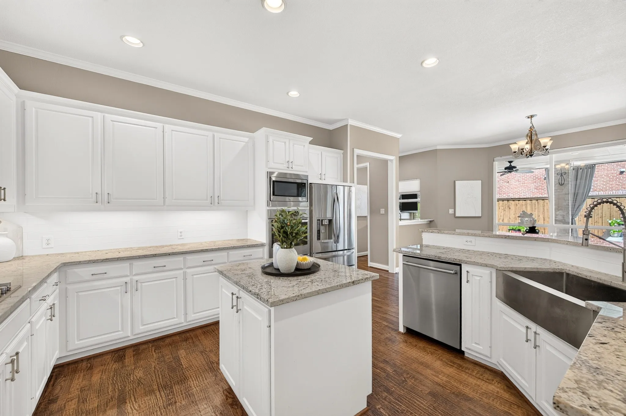 Kitchen featuring wood-finish flooring, white cabinetry, integrated stainless steel appliances, and a central island with a stone-finish countertop