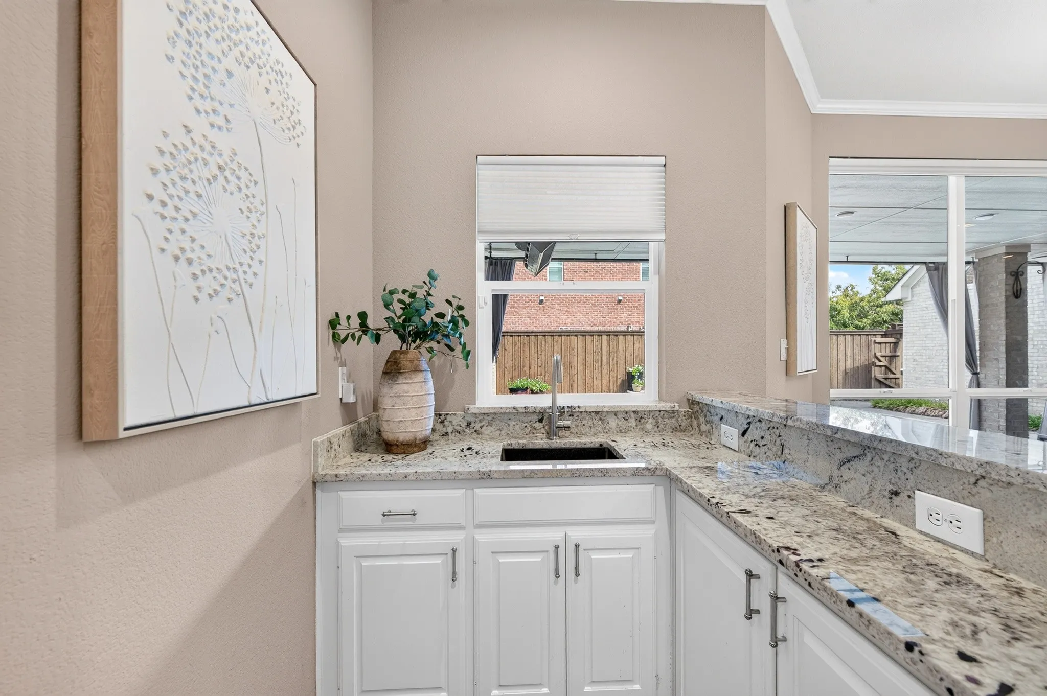 Built-in bar area featuring an undermount sink, light-colored cabinetry with dark hardware, and speckled stone countertops