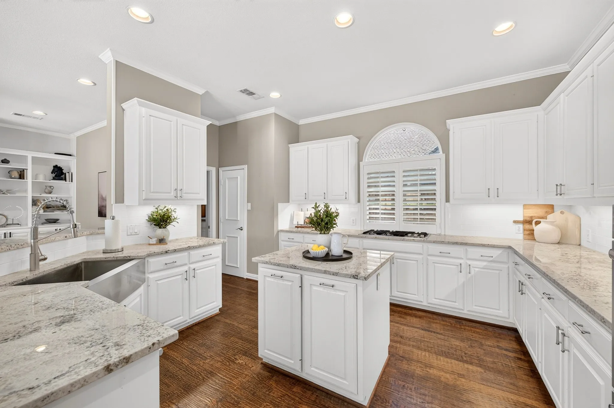 Kitchen featuring white cabinetry, light-toned countertops, a center island, hardwood flooring, and an arched window with plantation shutters
