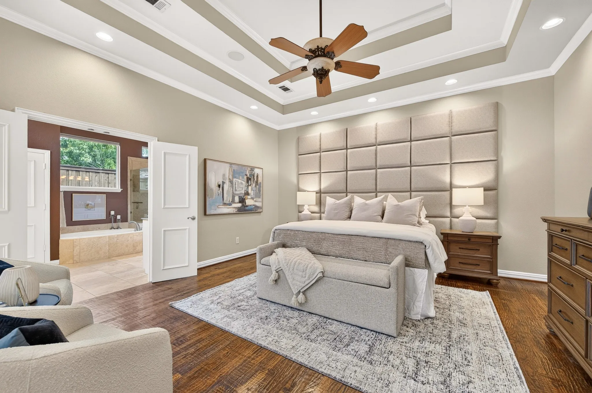 Wood-finish flooring, tray ceiling with recessed lighting, ceiling fan, and direct access to a full bathroom featuring a built-in tub