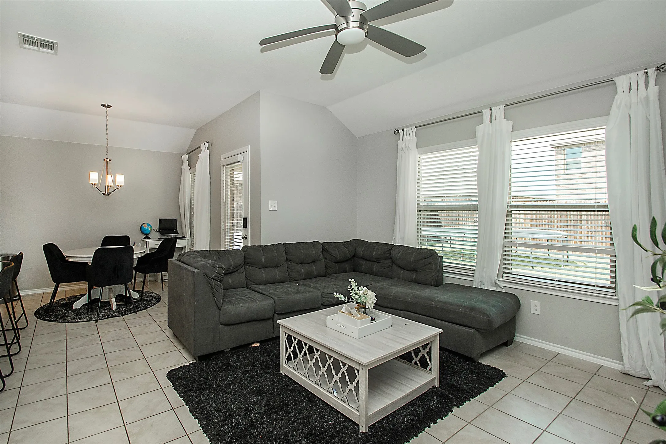 Open-concept living area featuring tile flooring, vaulted ceilings, and a ceiling fan