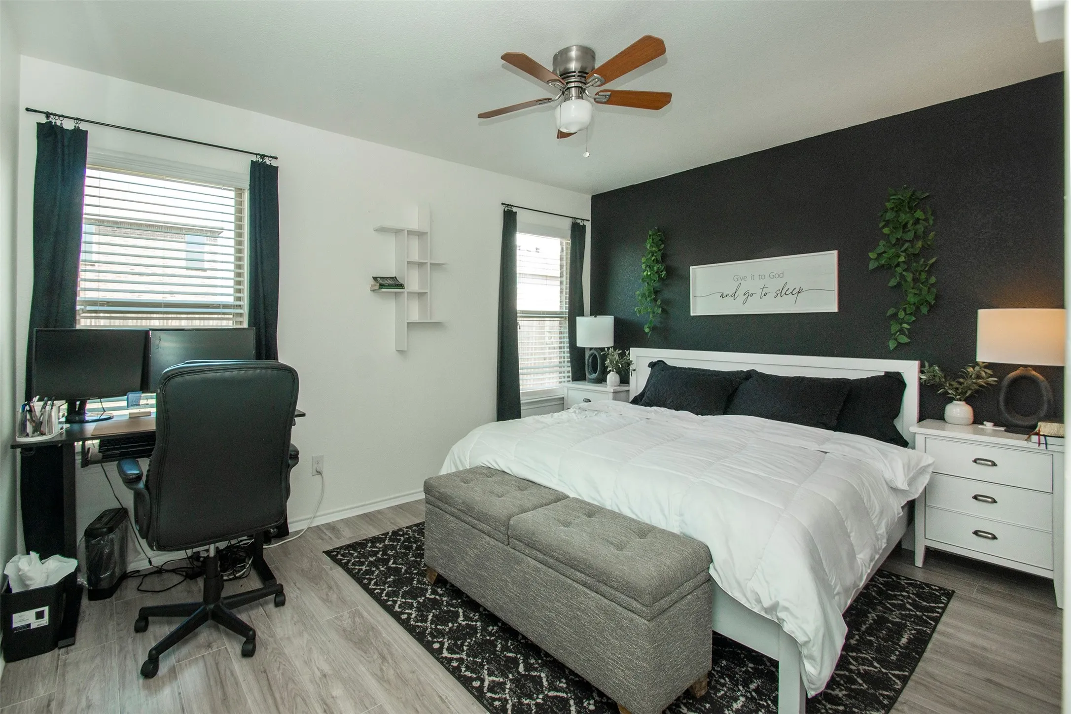 Bedroom featuring a contrasting accent wall, wood-finish flooring, and a ceiling fan with light fixture