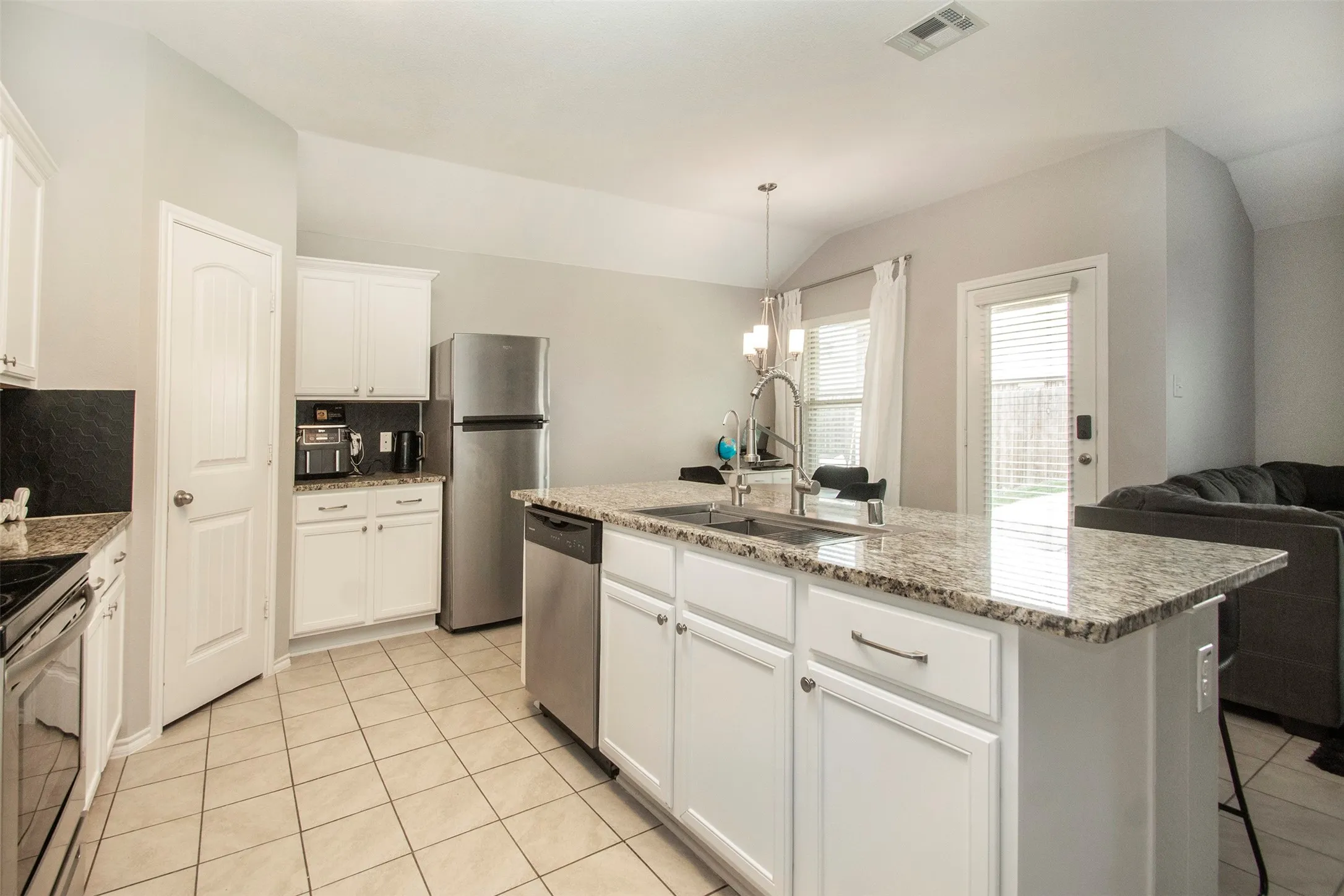 Modern kitchen featuring a central island with a granite countertop, undermount sink, and stainless steel dishwasher