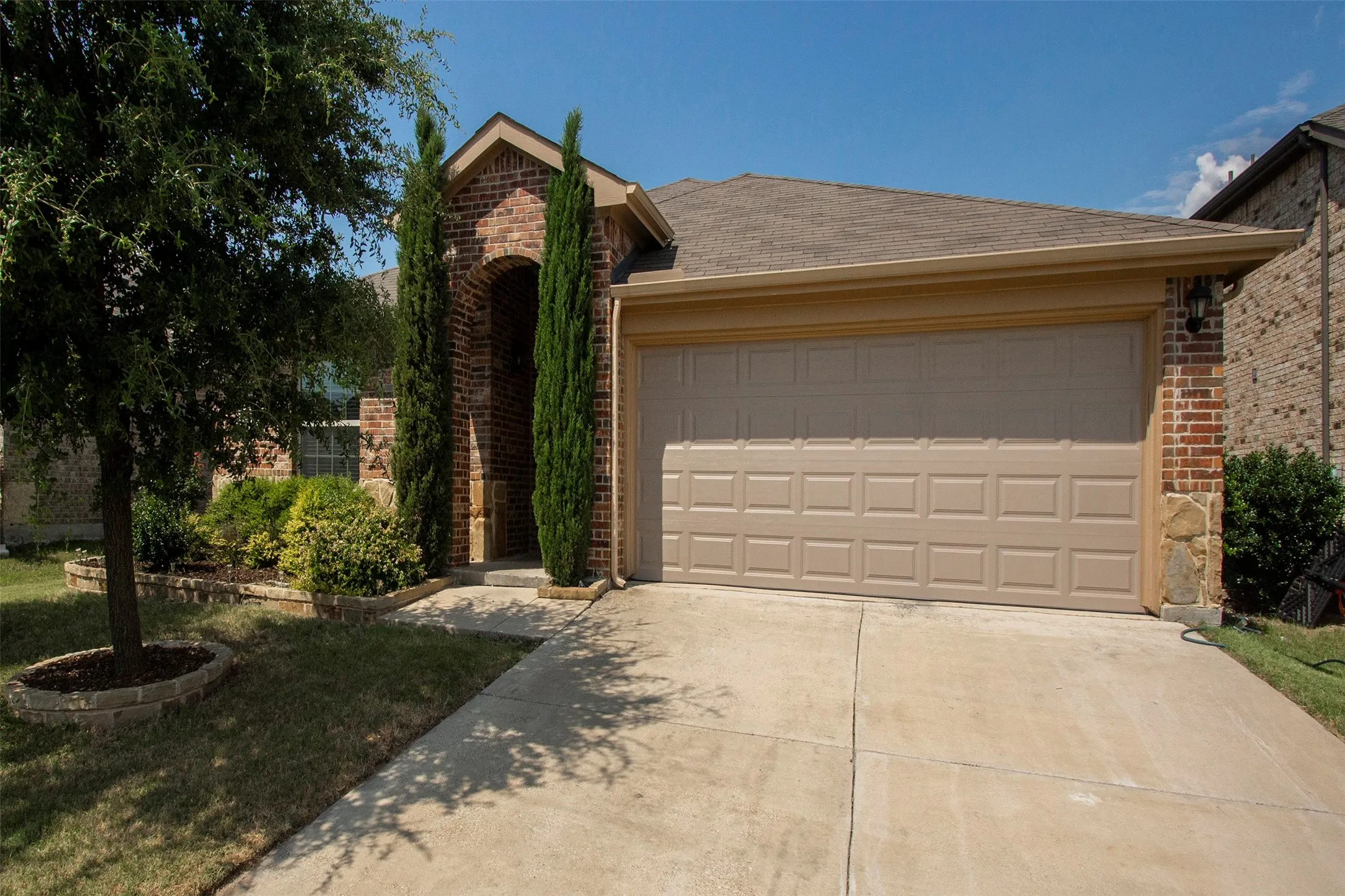Brick facade residence featuring a two-car garage, concrete driveway, and mature landscaping