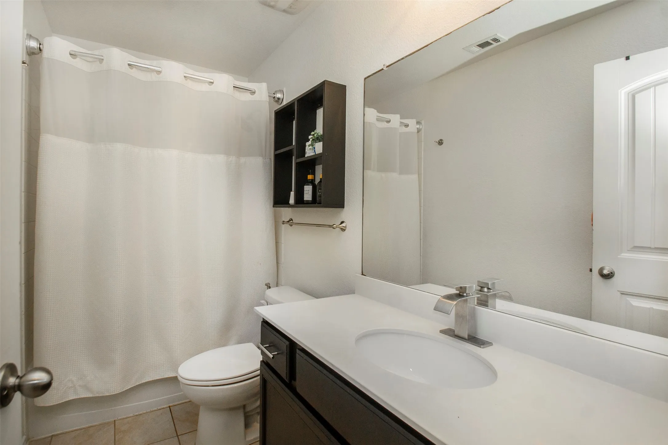 Bathroom featuring a spacious vanity with an undermount sink, a large wall-mounted mirror, a built-in dark wood shelving unit, and tiled flooring