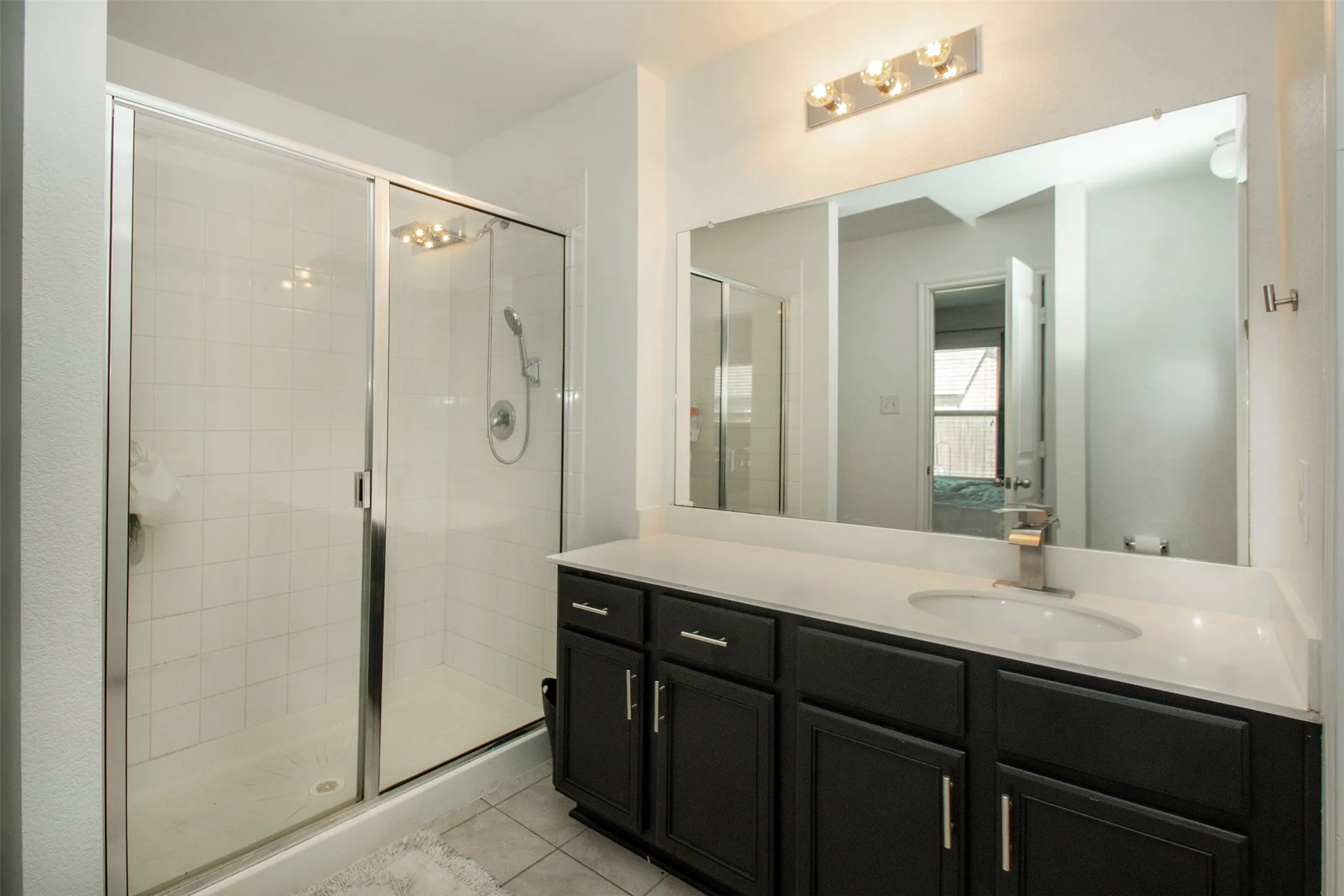 Bathroom featuring a glass-enclosed shower, dark wood-finish vanity with ample storage, white countertop, undermount sink, and a large wall-mounted mirror