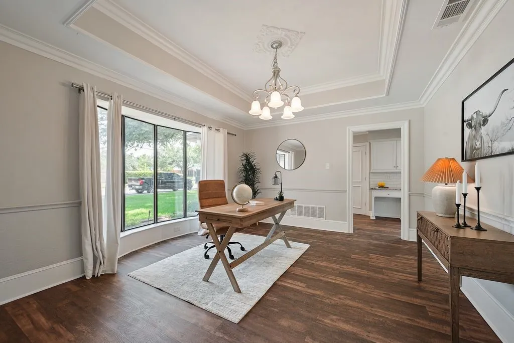 Spacious room featuring wood-finish flooring, a large bay window, and a tray ceiling with crown molding