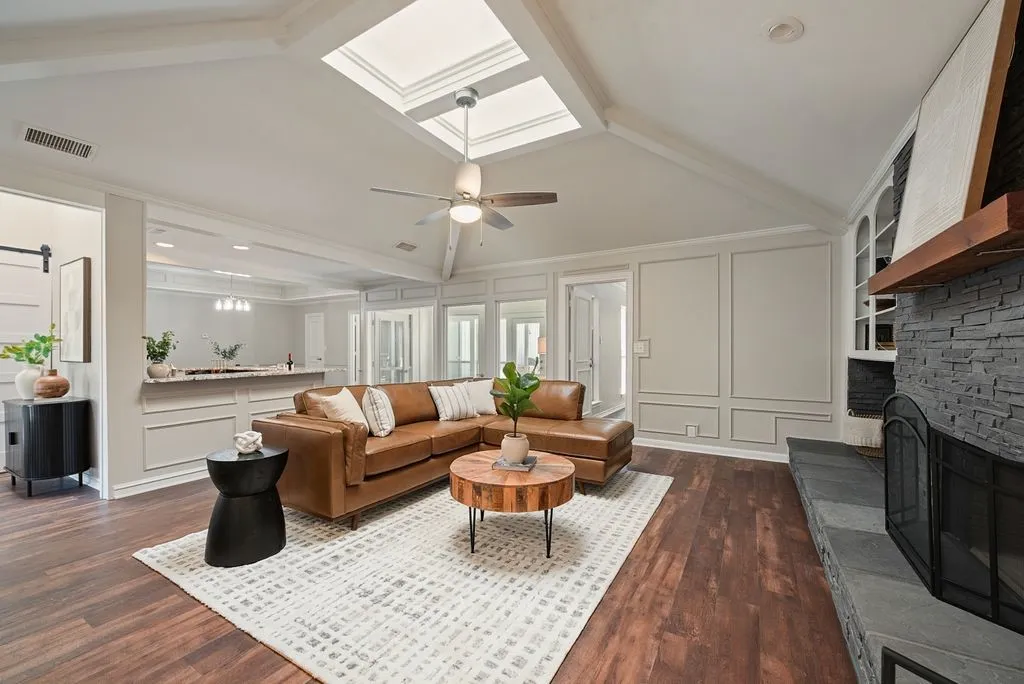 Spacious living room featuring vaulted ceilings, dual skylights, a stone-clad fireplace with a wood mantel, wood-finish flooring, and built-in shelving