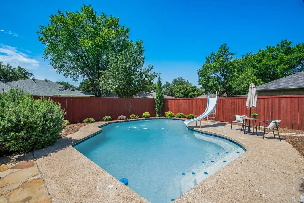 Backyard oasis featuring an in-ground swimming pool with a slide, surrounded by a concrete patio and a privacy fence