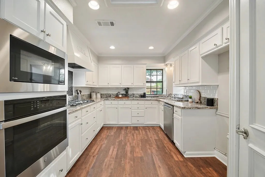 Kitchen featuring wood-finish flooring, white cabinetry, granite countertops, and stainless steel appliances