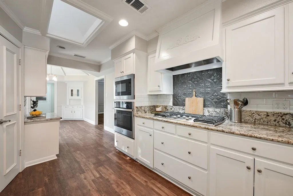 Kitchen featuring white cabinetry, granite countertops, a gas range with a decorative hood, a tile backsplash, and wood-finish flooring