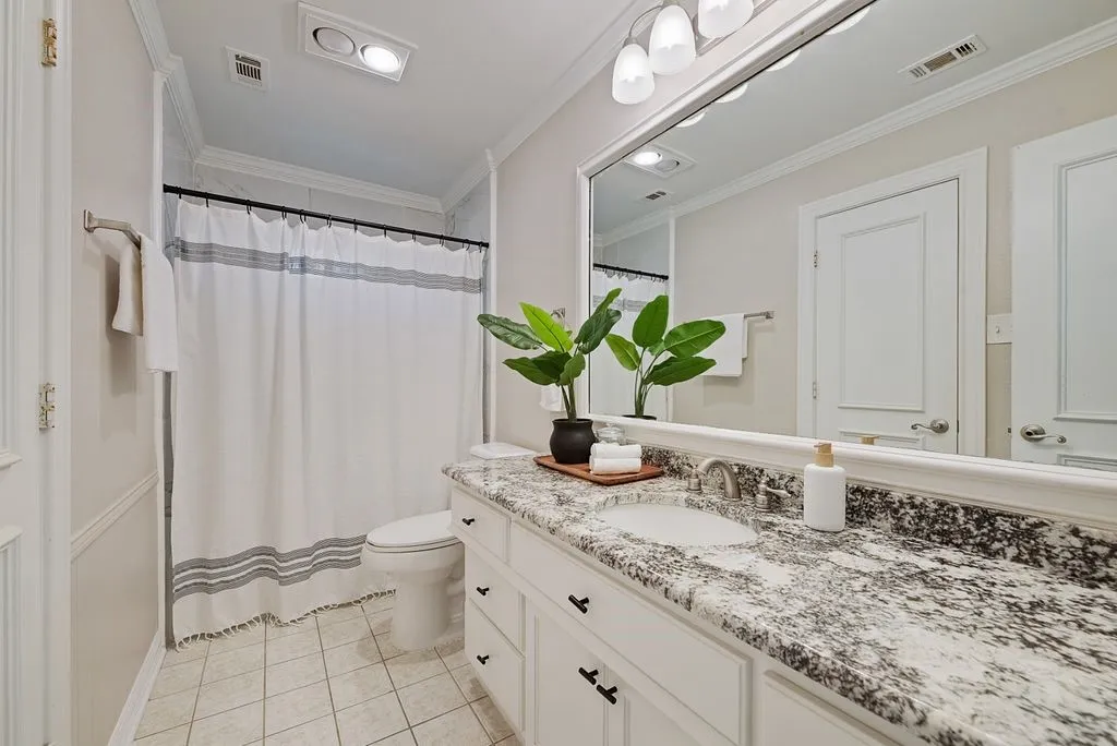 Vanity featuring a stone countertop with an integrated sink, polished chrome faucet, and white cabinetry with dark hardware