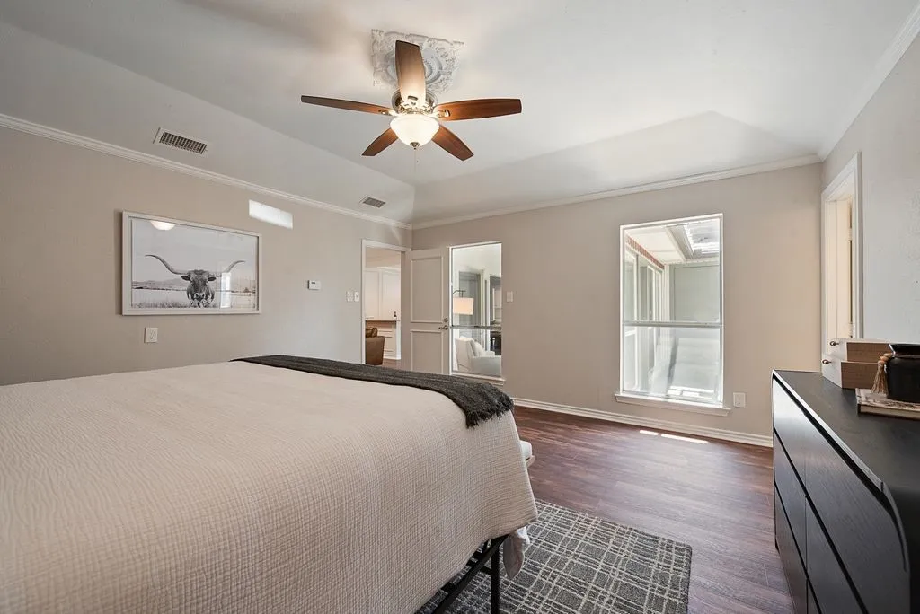 Bedroom featuring wood-finish flooring, a tray ceiling with a ceiling fan, and crown molding