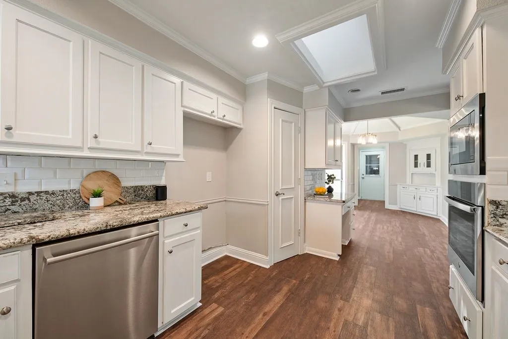 Kitchen featuring white cabinetry, granite countertops, stainless steel appliances, wood-finish flooring, and a ceiling skylight