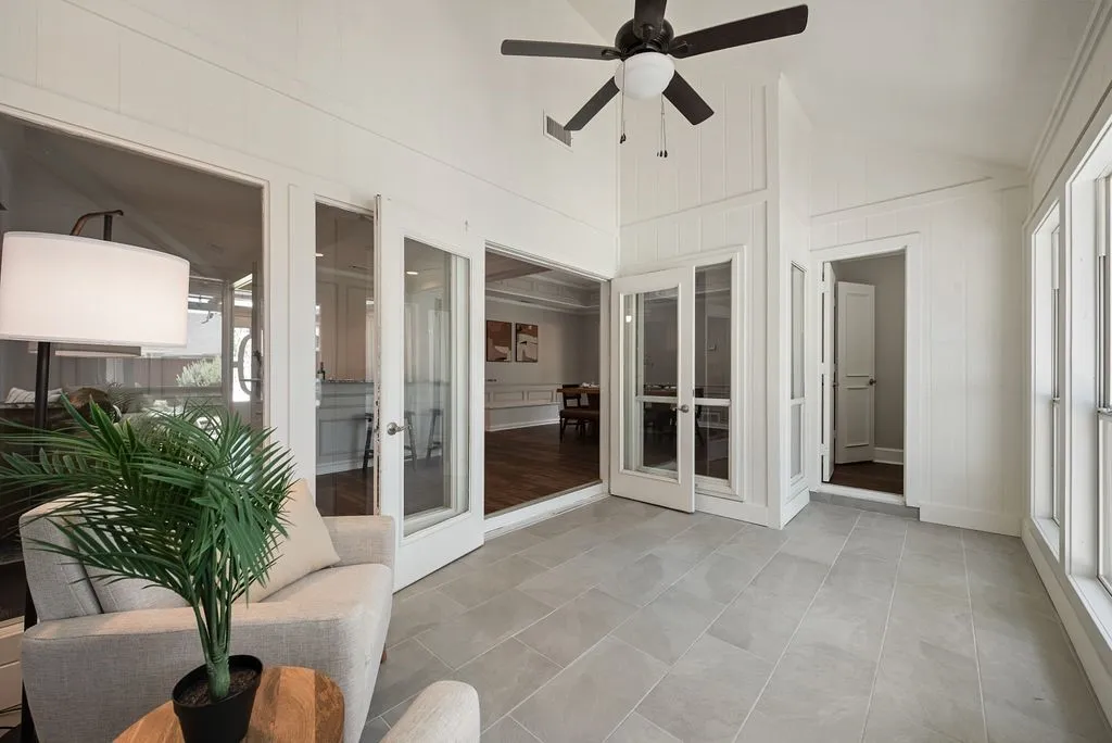 Sunroom with light-toned tile flooring, white vertical wall paneling, and a dark-toned ceiling fan