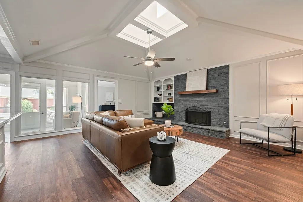Living area featuring wood-finish flooring, vaulted ceiling with exposed beams and skylights, and a ceiling fan