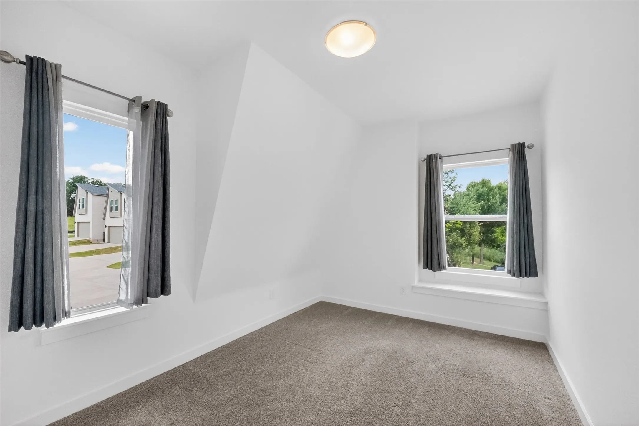 Carpeted room with white walls, two windows with window treatments, and a ceiling-mounted light fixture