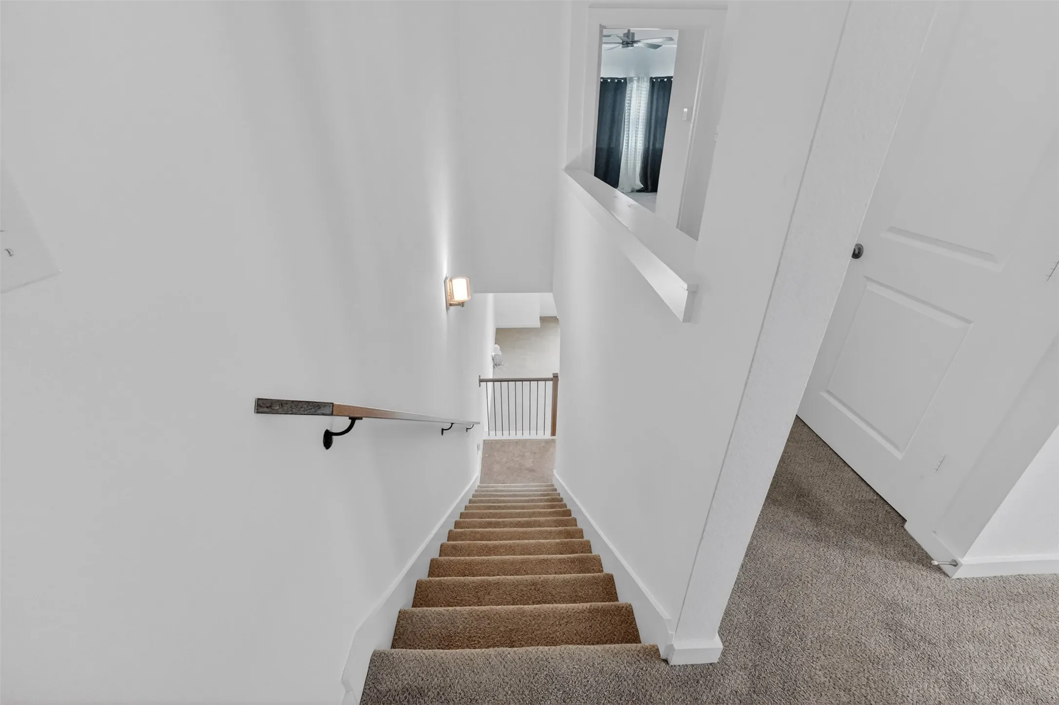 Carpeted staircase with a wood handrail featuring metal brackets, leading to an upper landing with white walls and a white paneled door