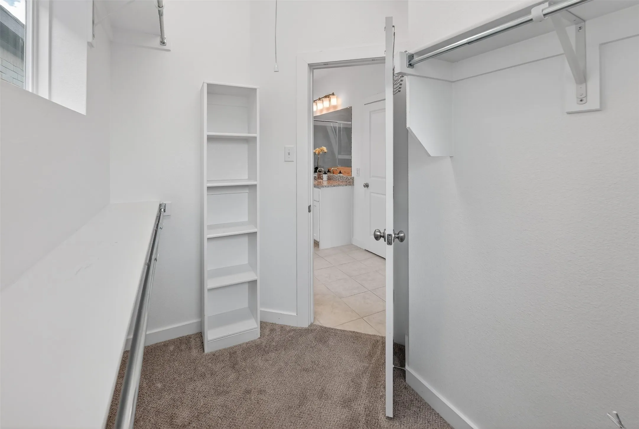 Walk-in closet featuring built-in shelving, carpet flooring, a clothing rod system, and direct access to a bathroom with tile flooring