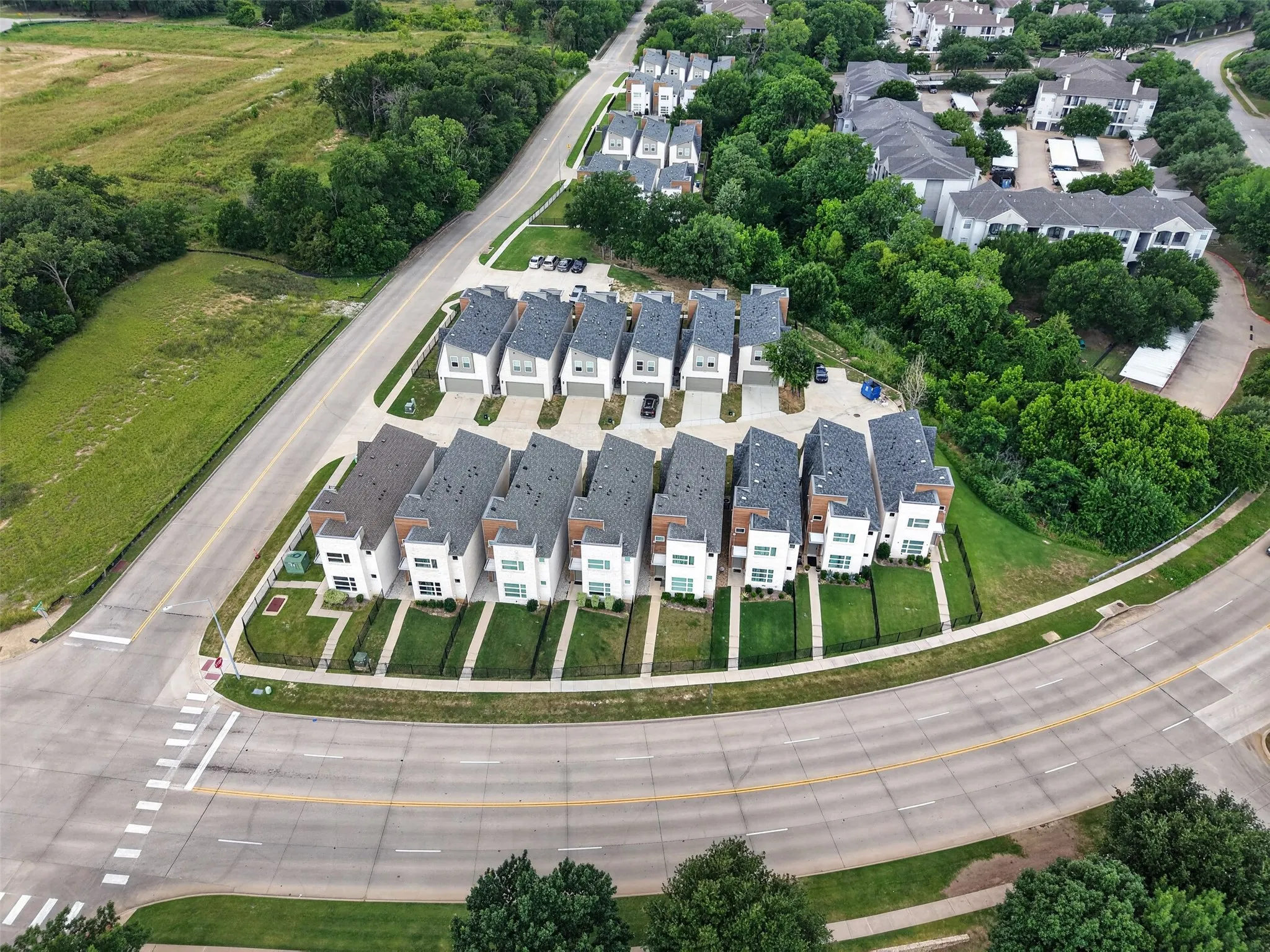 Contemporary townhome development featuring light-colored facades, dark roofs, individual attached garages, manicured front lawns, and paved pathways
