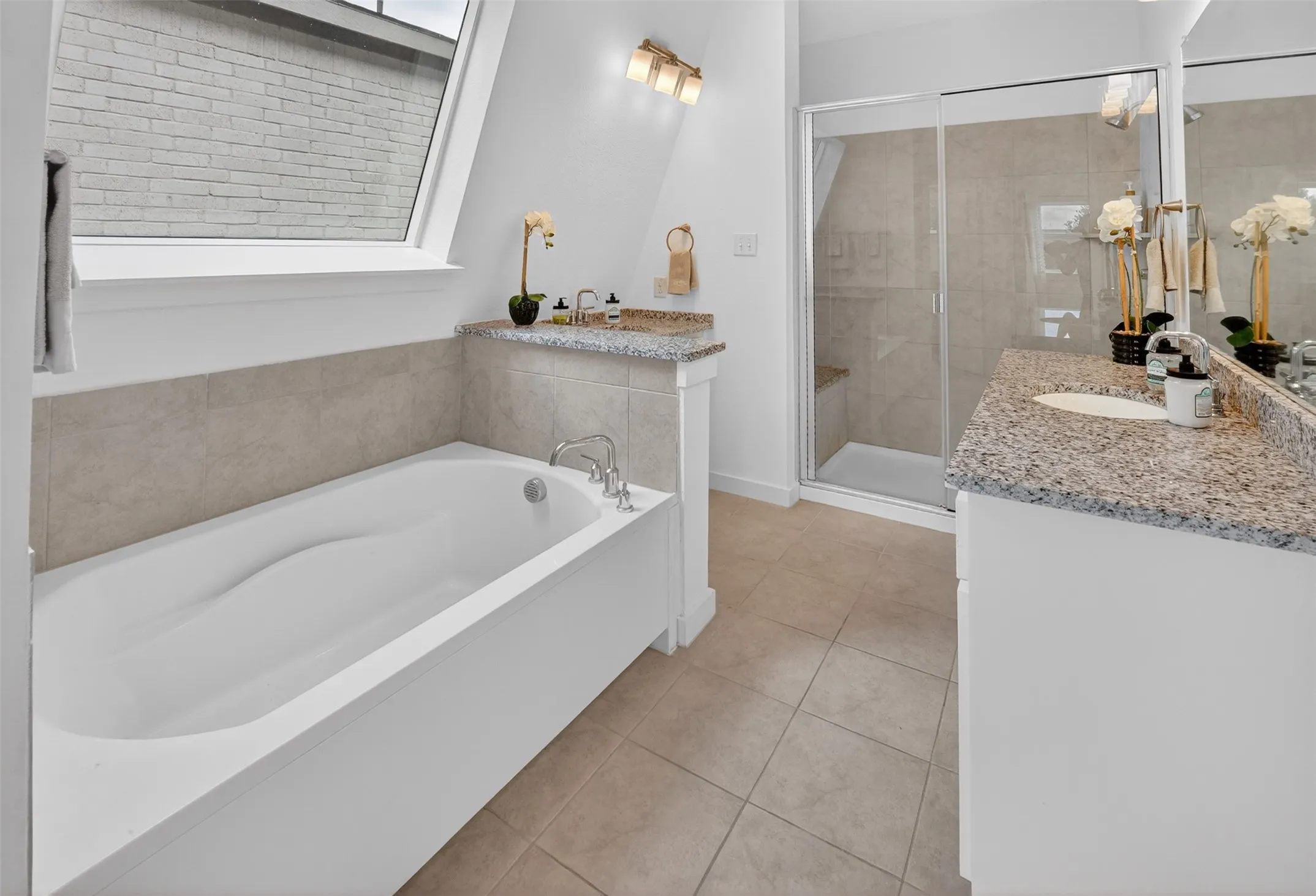Modern bathroom featuring a soaking tub, a separate glass-enclosed shower, dual vanities with granite countertops, and tiled flooring