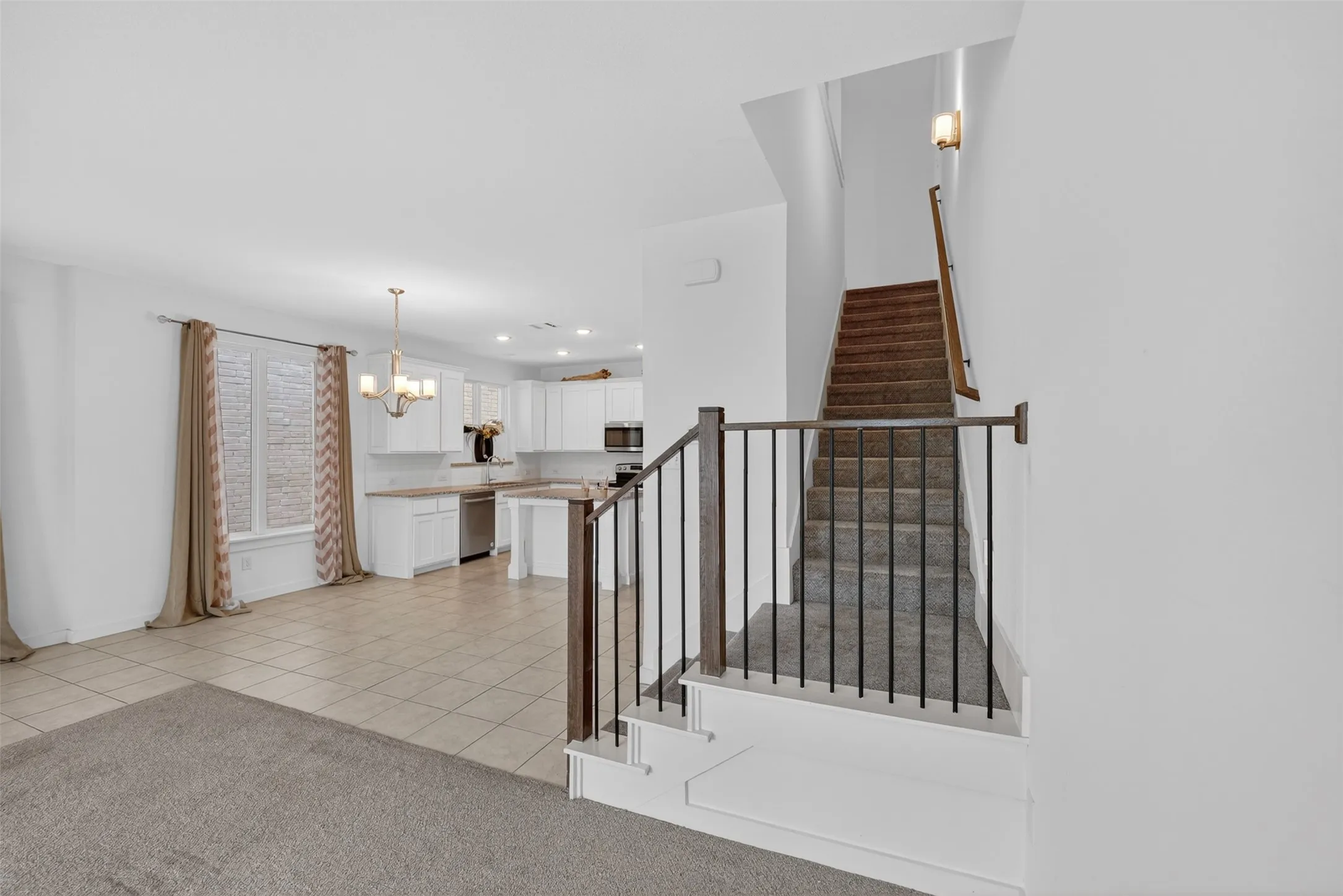 Open-concept living space featuring a staircase with wood-finish handrails and black metal balusters, tiled flooring, white cabinetry, a built-in microwave, and a chandelier