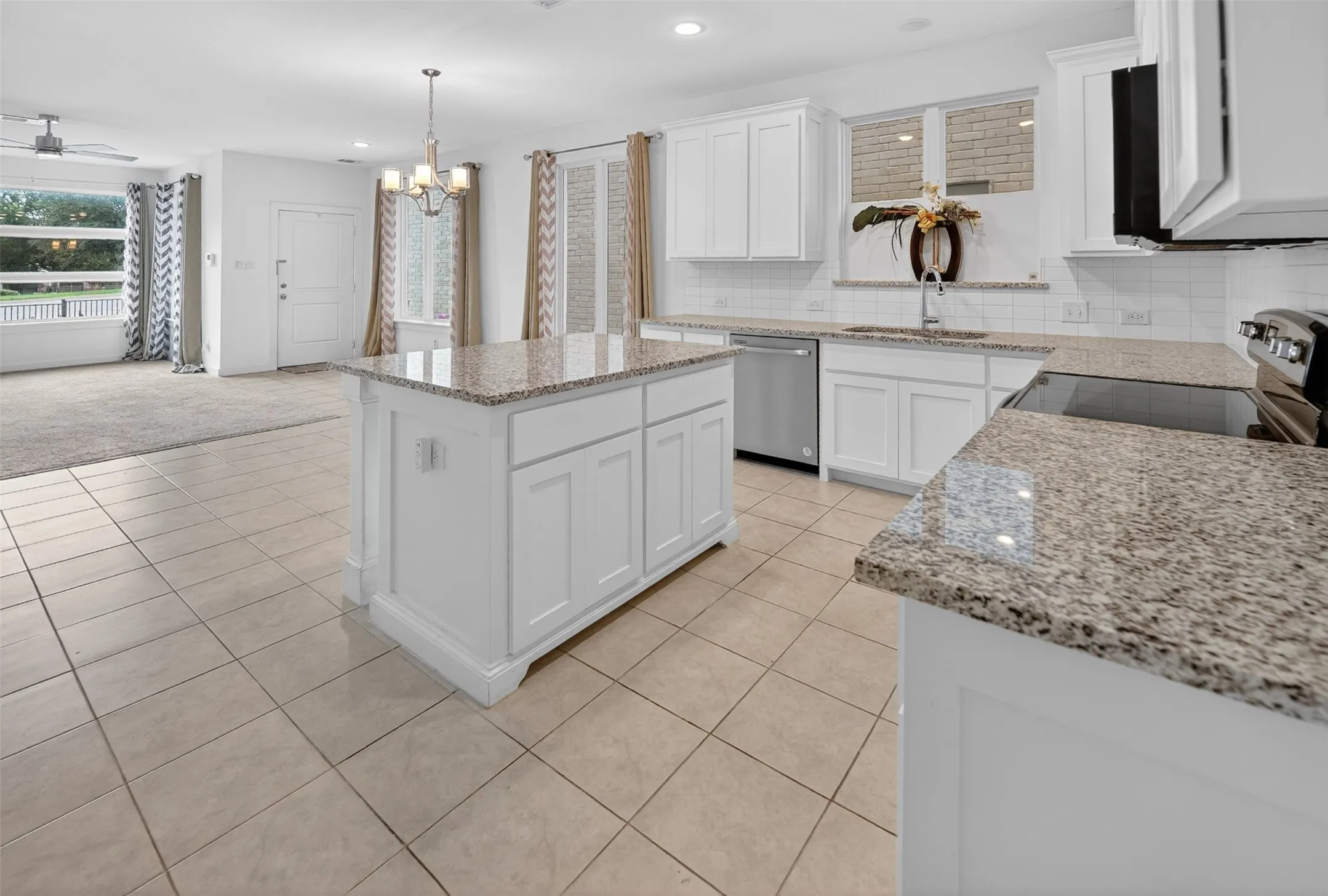 Kitchen featuring a central island with a granite countertop, white cabinetry, integrated stainless steel dishwasher, and a black electric cooktop