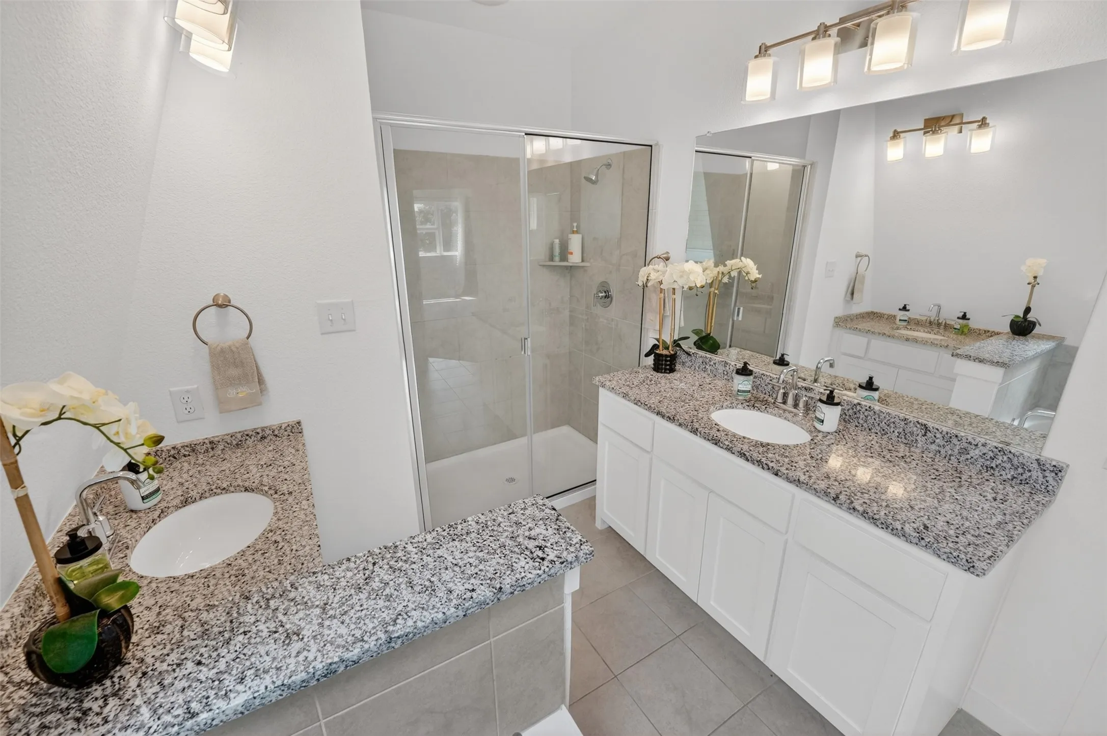 Bathroom featuring a frameless glass shower enclosure, dual vanities with speckled countertops, under-mount sinks, and white cabinetry