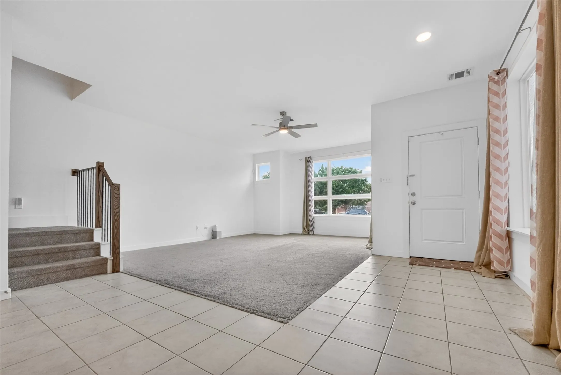 Open-concept living space featuring a tiled entryway, neutral carpeting, large windows, and a ceiling fan