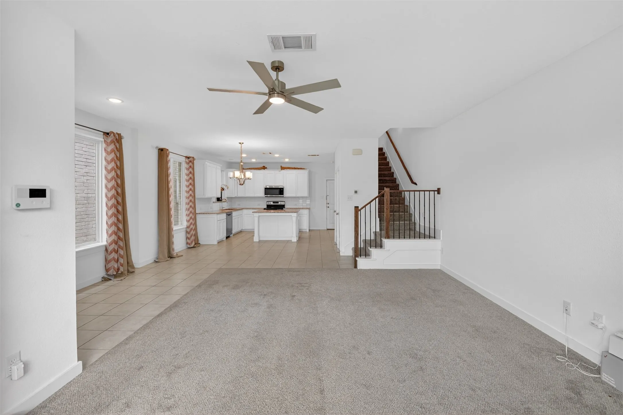 Open-concept living space featuring light-colored carpeting and tile flooring