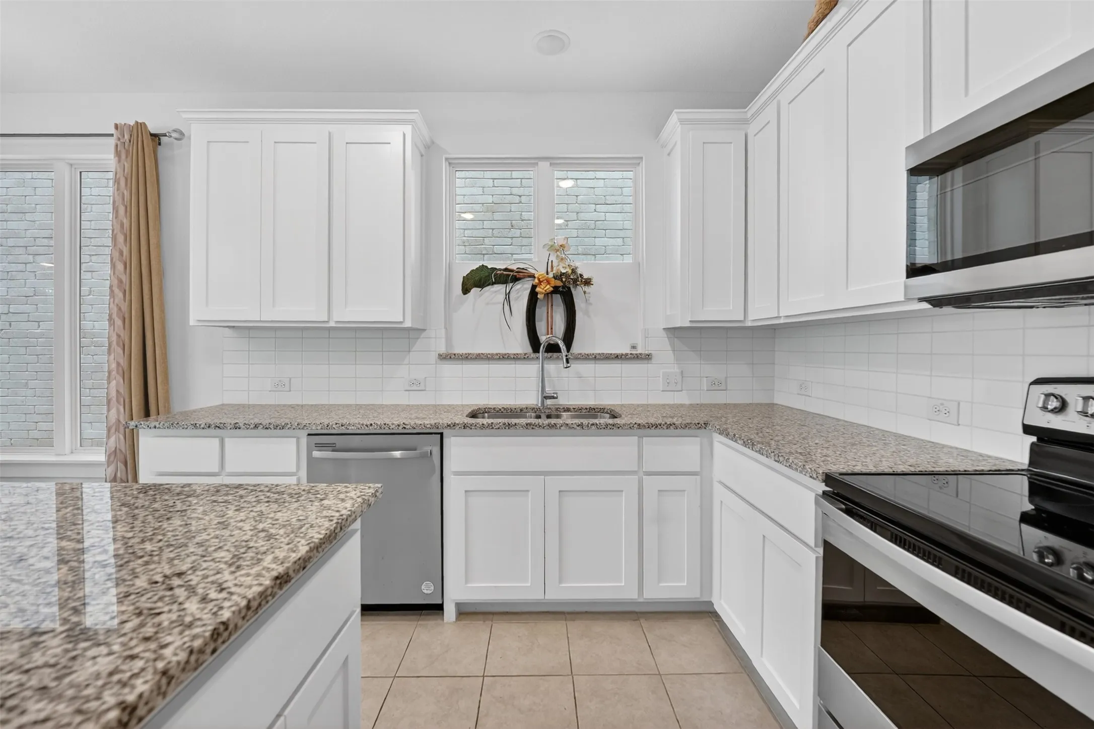 Bright kitchen featuring white shaker-style cabinetry, granite countertops, a white subway tile backsplash, stainless steel appliances, and tile​​‌​​​​‌​​‌‌​‌‌​​​‌‌​‌​‌​‌​​​‌​​ flooring