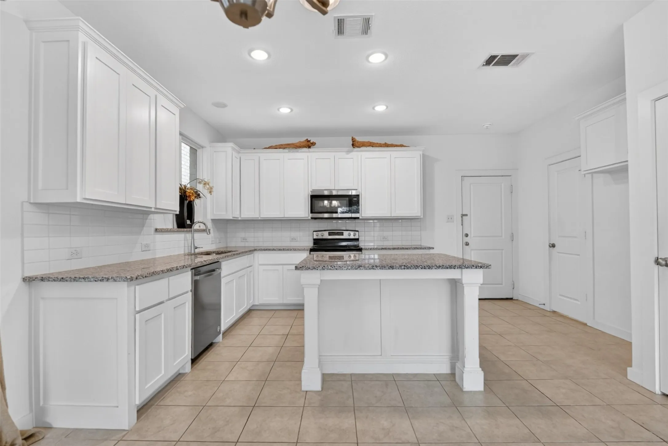 Contemporary kitchen featuring white cabinetry, light-toned tile flooring, speckled countertops, a center island, and stainless steel appliances