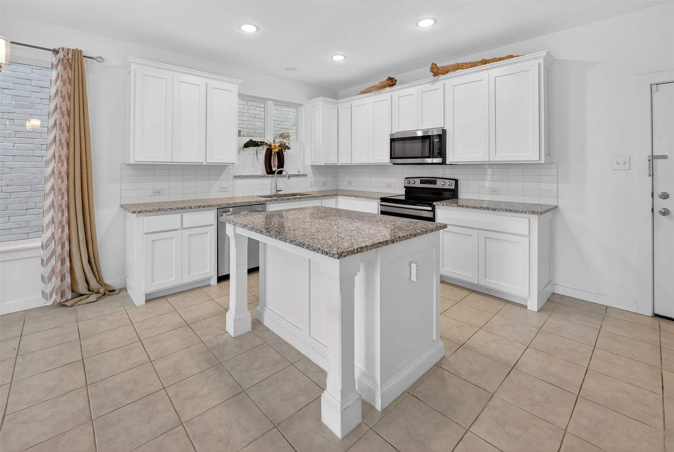 Kitchen featuring an island, white cabinetry, granite countertops, subway tile backsplash, and recessed lighting