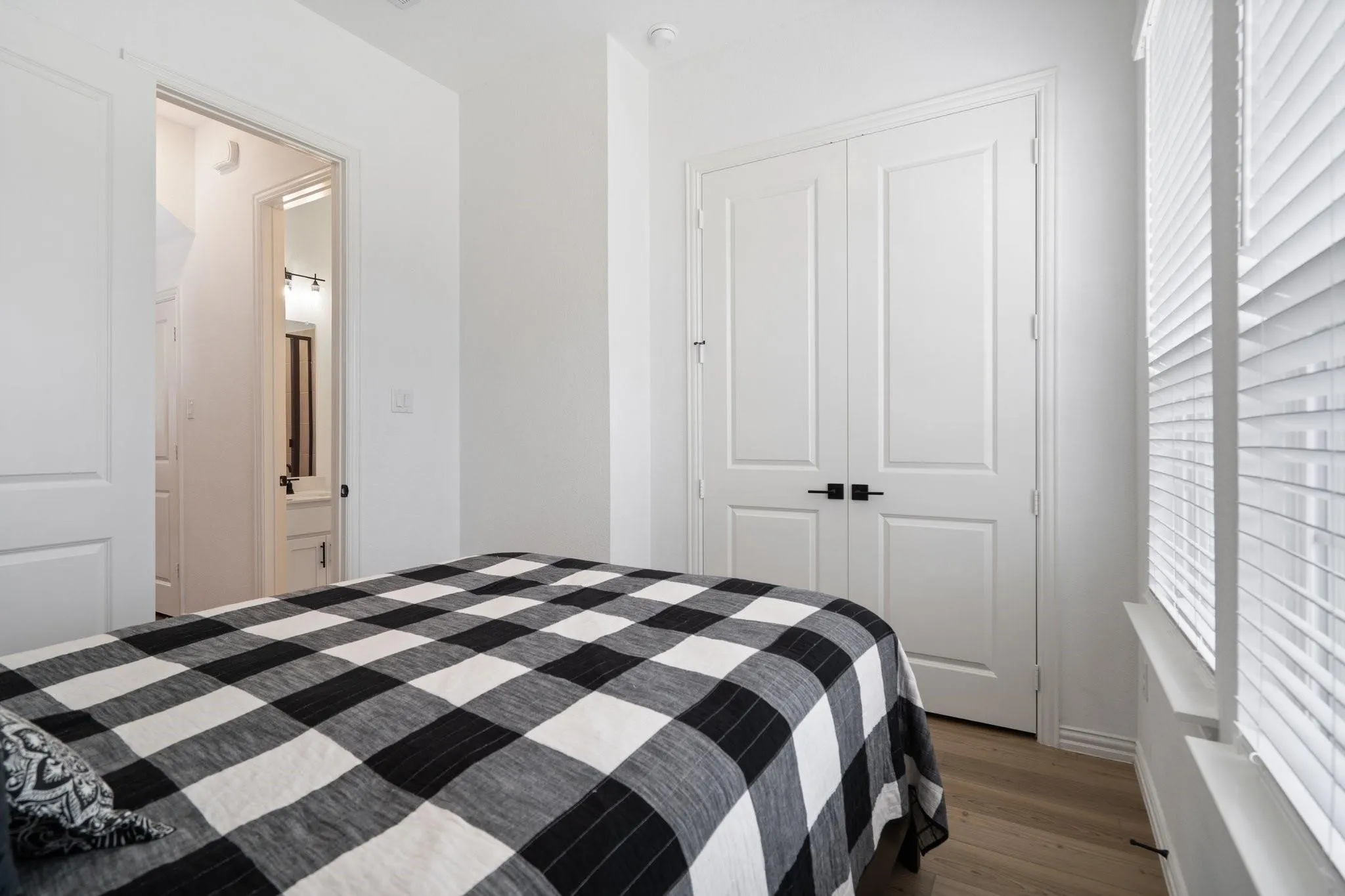 Parent's Bedroom featuring wood-finish flooring, white paneled doors with black hardware, and a window with horizontal blinds